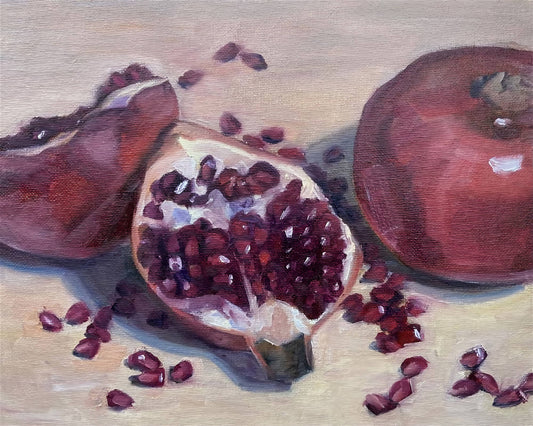 Two pomegranates on a beige background.  One pomegranate is split open, red seeds are spilling out.